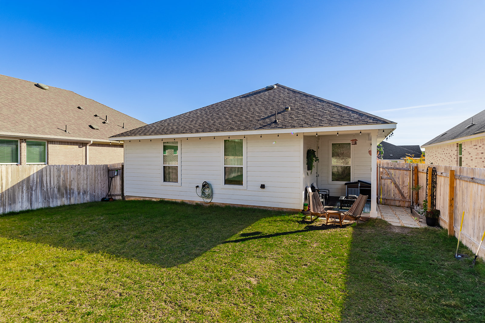 Rear exterior — single-story home with covered patio, string lights and fenced backyard