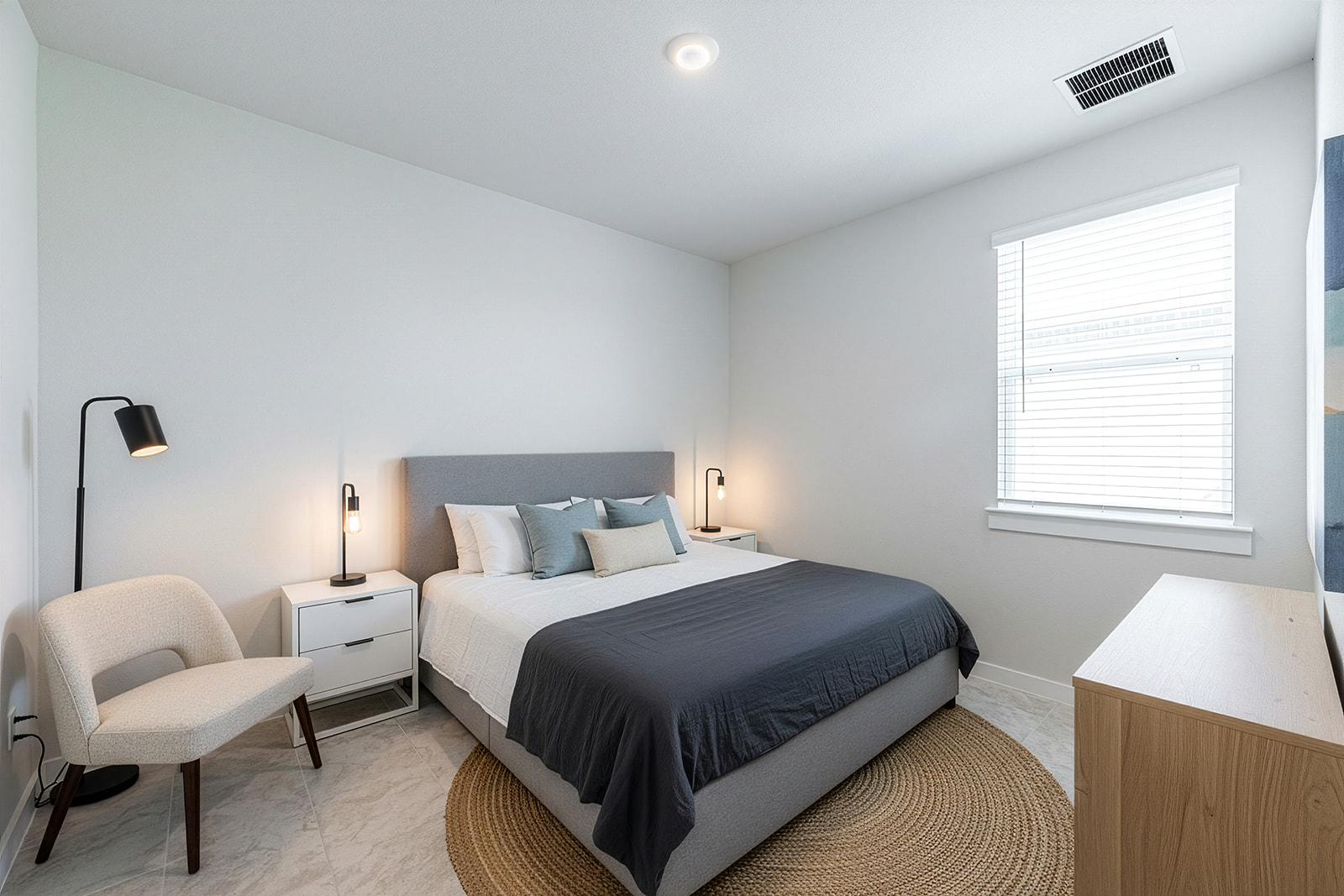 Guest bedroom with gray upholstered bed, jute rug, accent chair and natural light