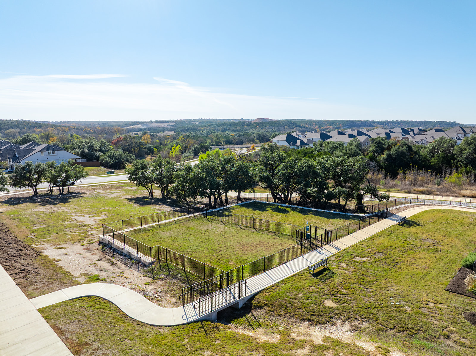Community dog park with shaded oak trees and Hill Country views