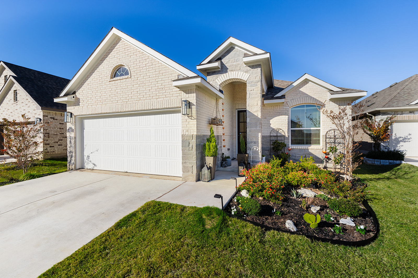 Front exterior — white brick with stone accents, 2-car garage, arched entry and landscaped flower beds