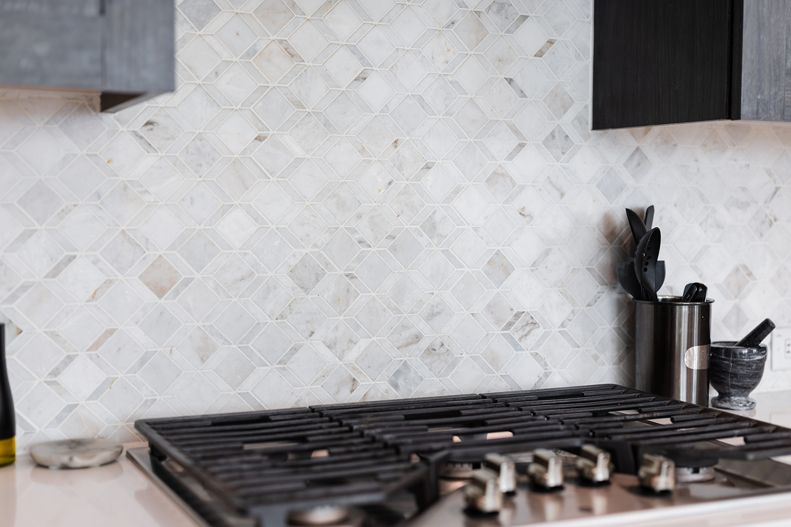 Designer marble diamond-pattern backsplash detail with built-in gas range and dark cabinets