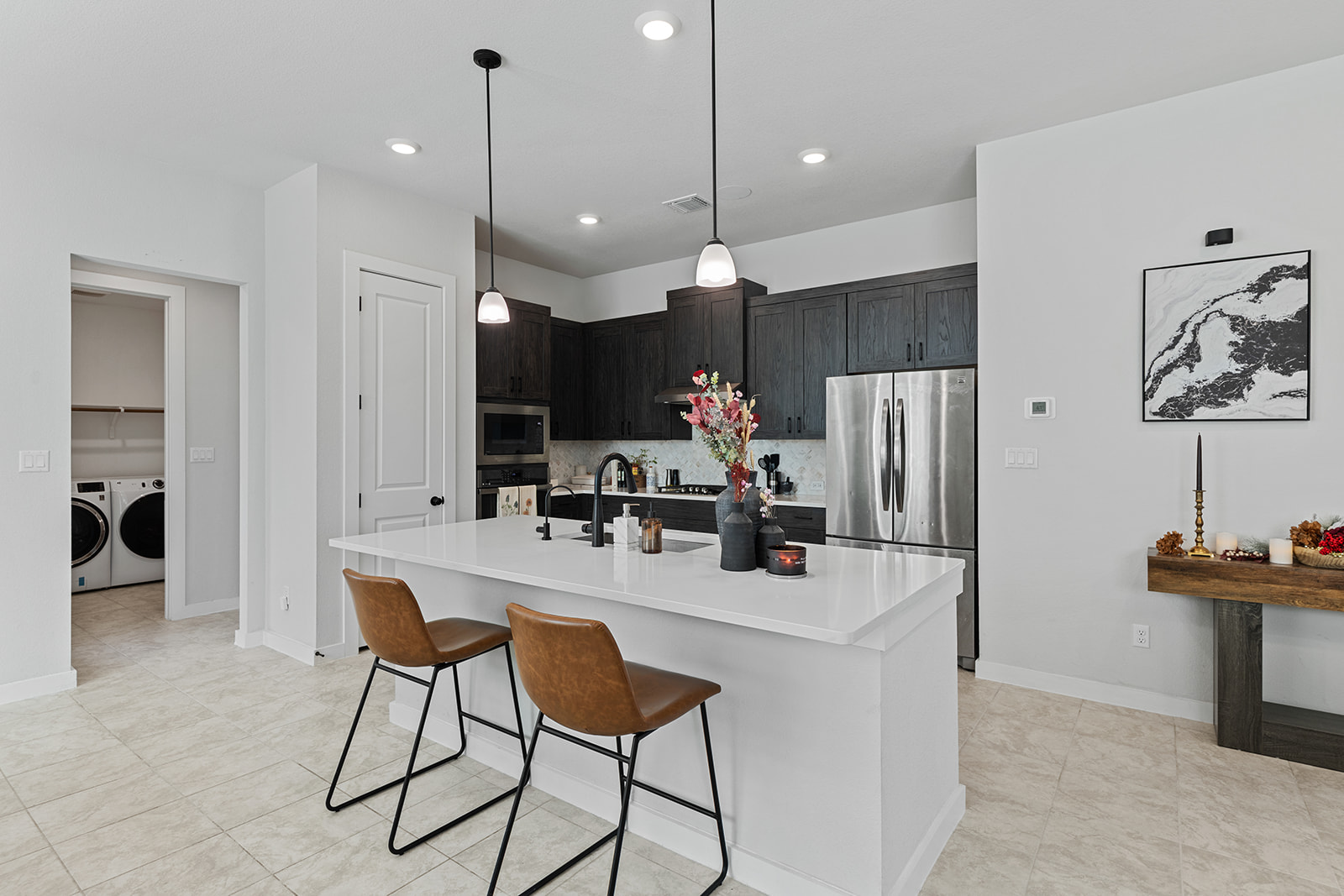 Kitchen island with pendant lights, leather stools, laundry room view and built-in oven