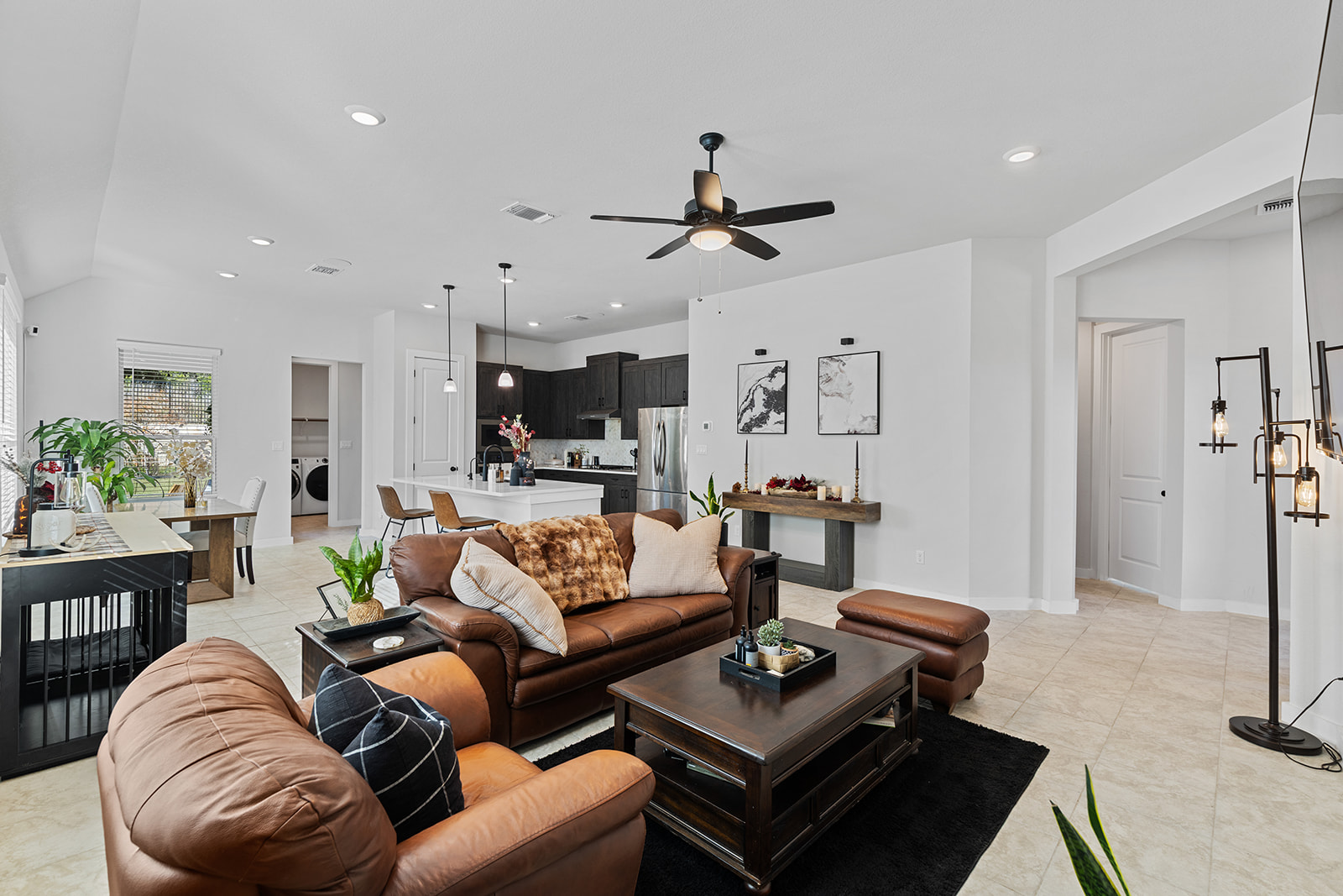 Open floor plan — living room with leather furniture, dining area, kitchen island and pendant lights