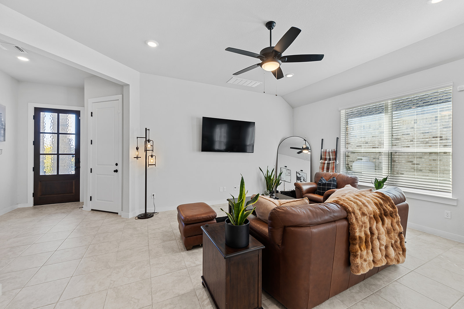 Living room with wall-mounted TV, leather sofa, entry door and industrial floor lamp