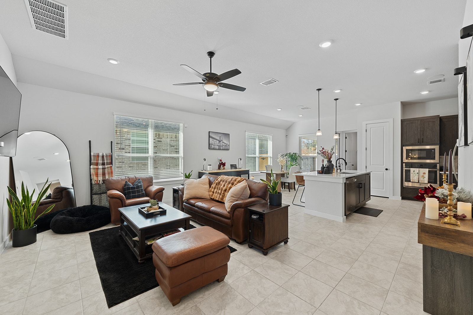 Open-concept living room with leather sofas, ceiling fan, kitchen island and recessed lighting