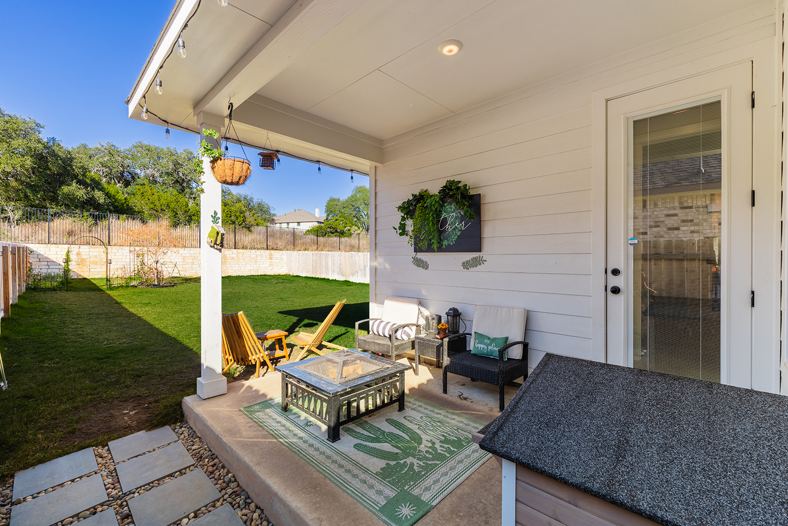 Covered patio with seating area, fire pit, string lights and greenbelt backyard views