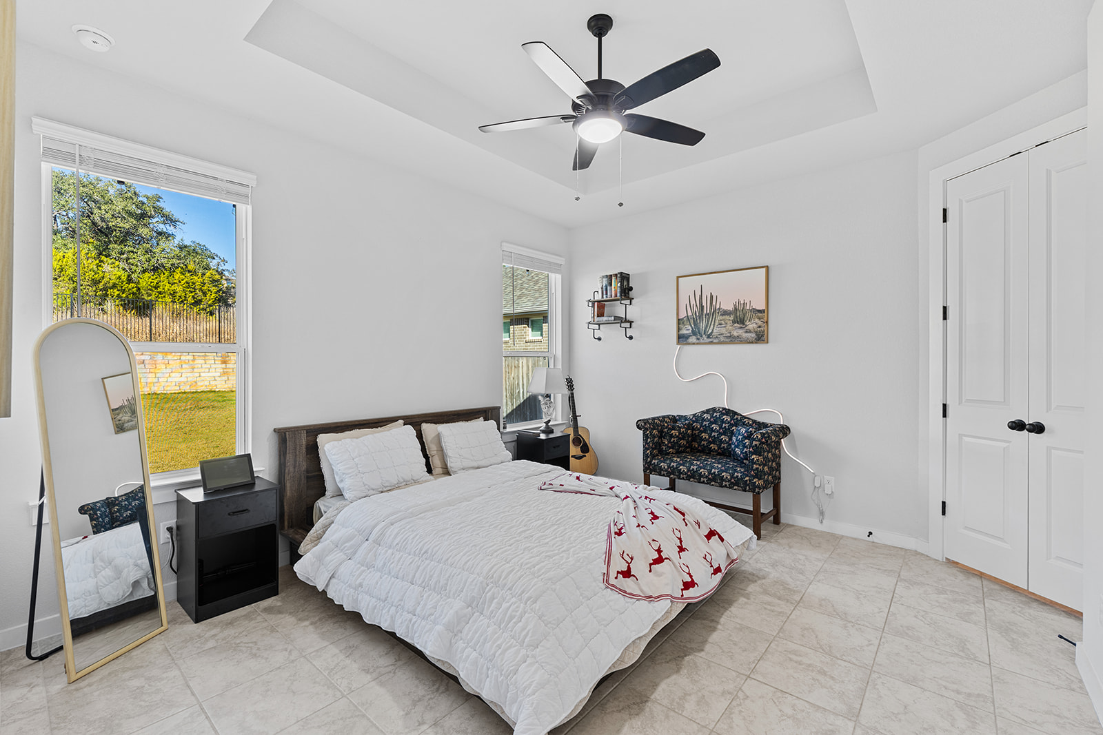 Primary bedroom with tray ceiling, ceiling fan, backyard window view, guitar and desert art